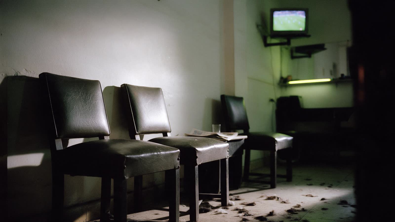 El rincón de espera del local: tres sillas de cuero gastado, un diario doblado y el televisor prendido pasando un partido.